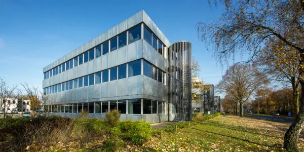 Modern kantoorgebouw aan de Huis ter Heideweg met metalen gevel en grote ramen, gelegen langs een boomrijke straat.